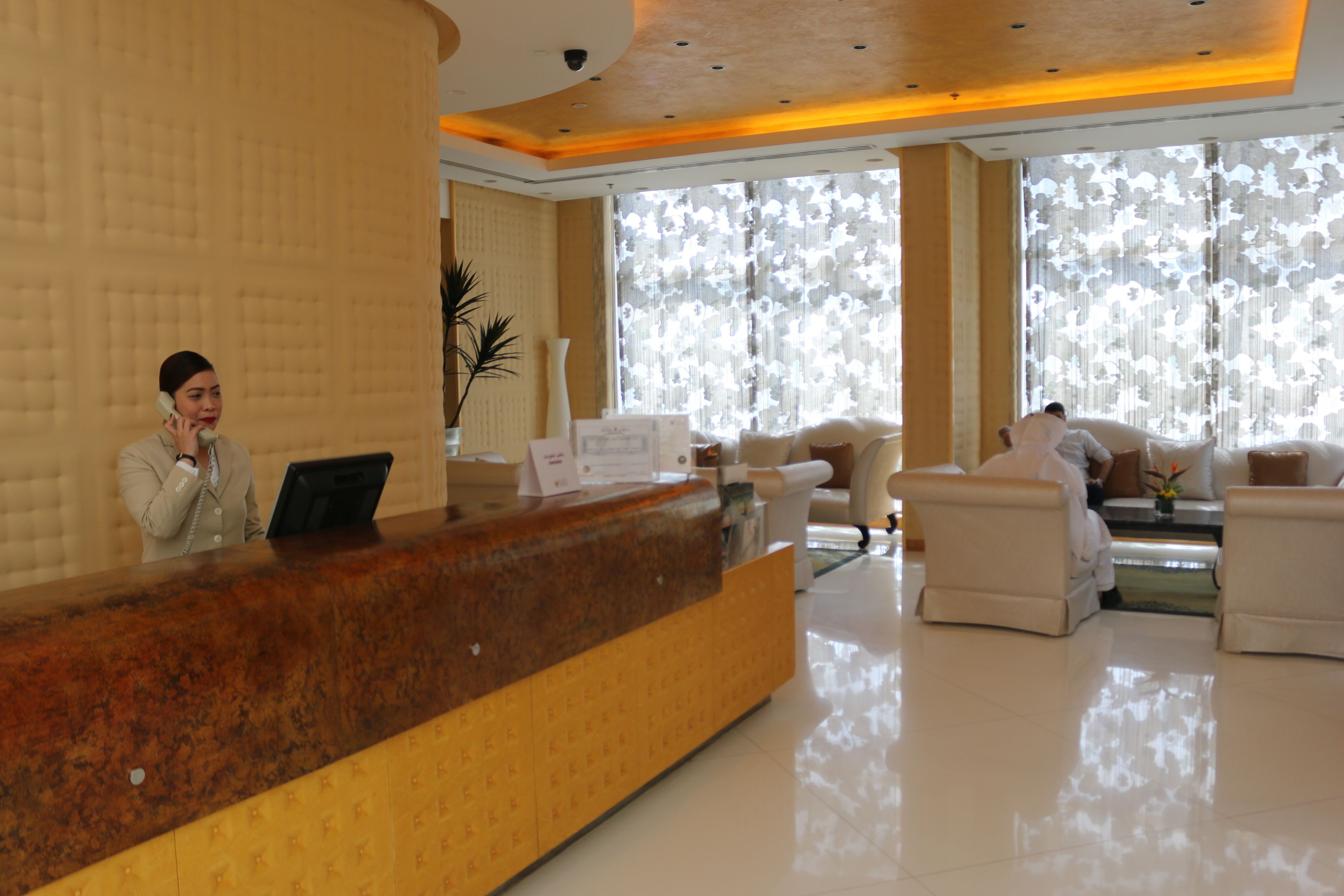 A hotel reception area with a marble counter, a receptionist, and a seating area with two sofas and a coffee table.