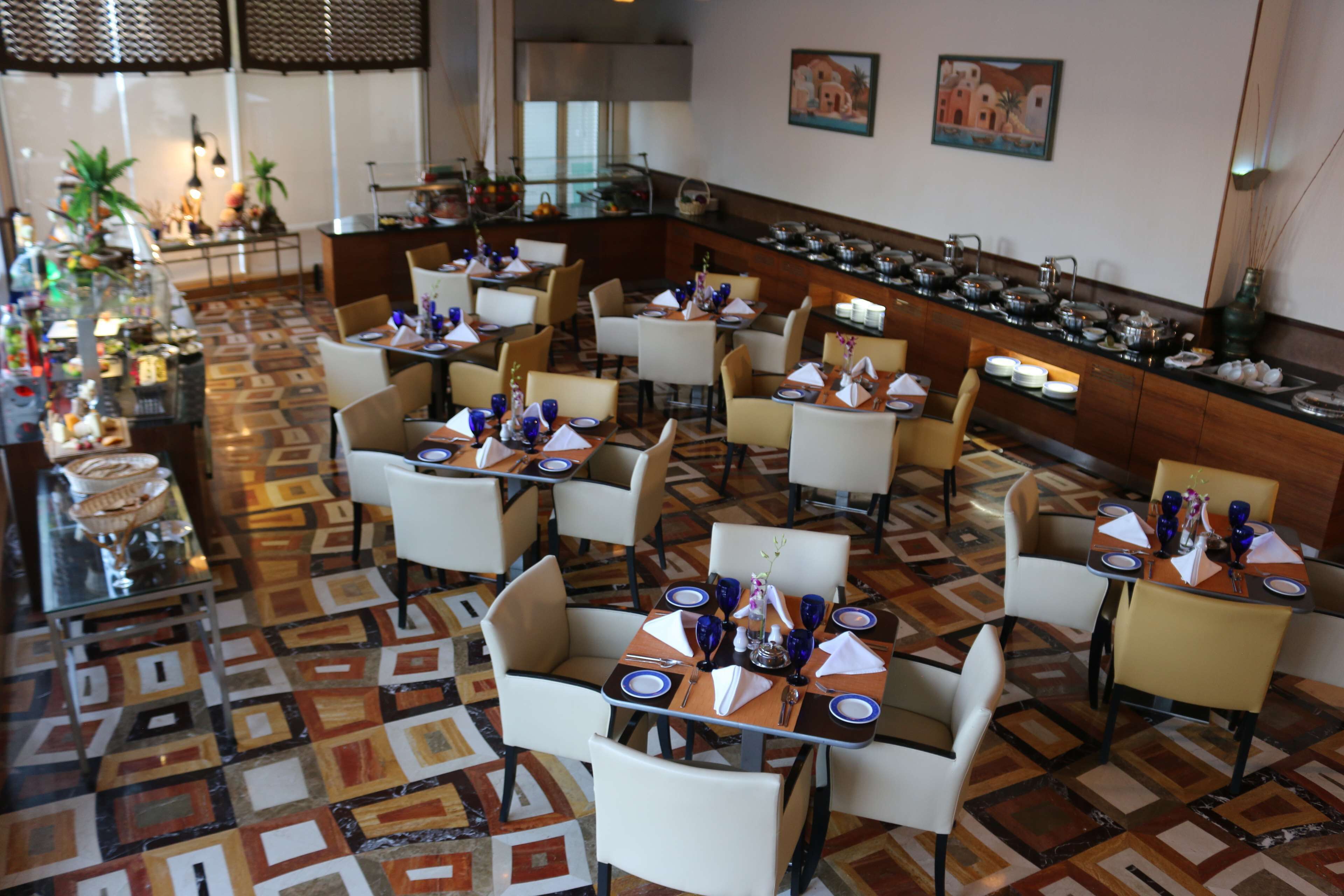 Ein Restaurant mit mehreren Tischen und Stühlen, einem gemusterten Boden und einem Buffet mit verschiedenen Speisen.