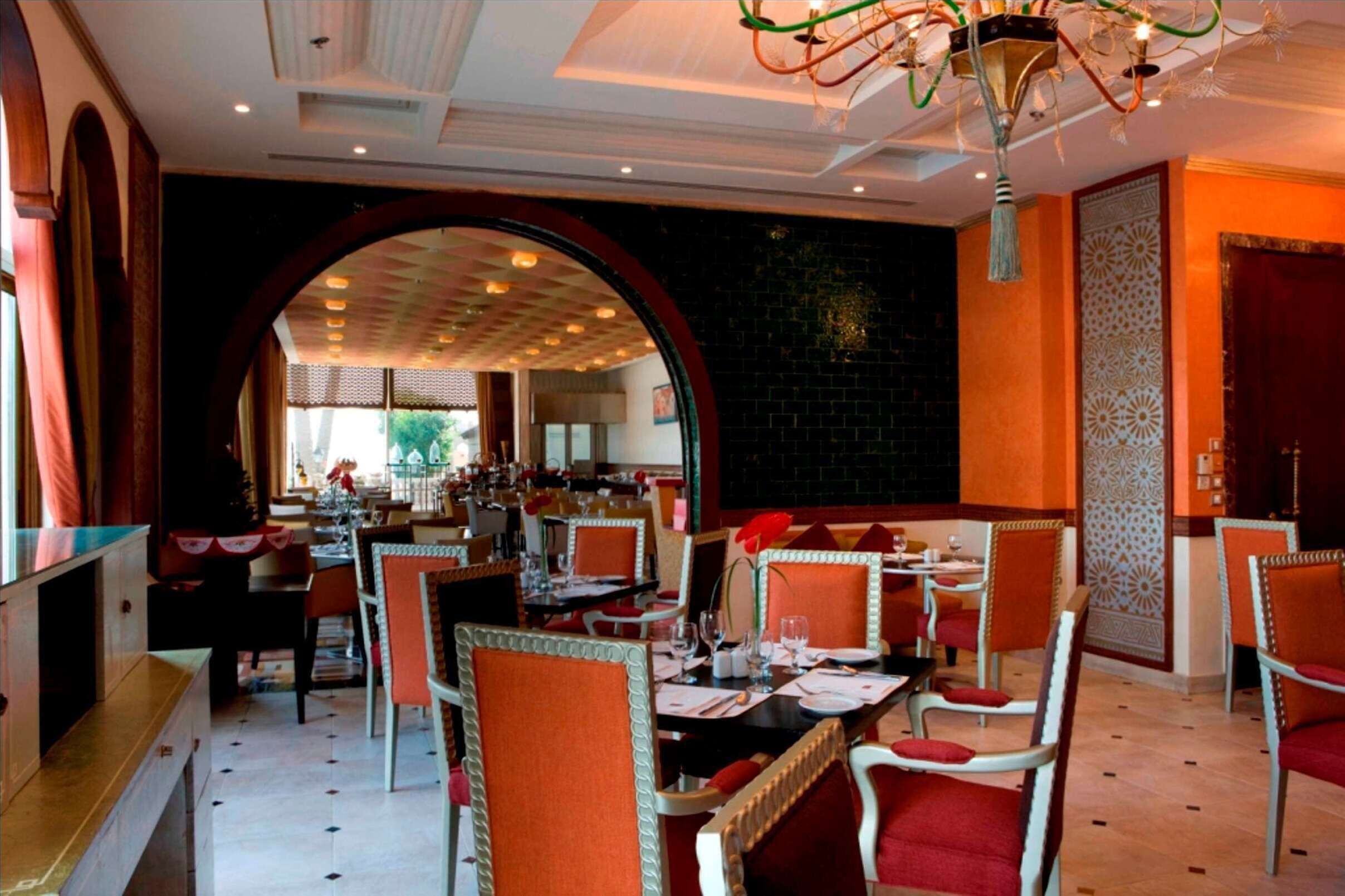 A restaurant with tables and chairs, a chandelier, and a large archway.