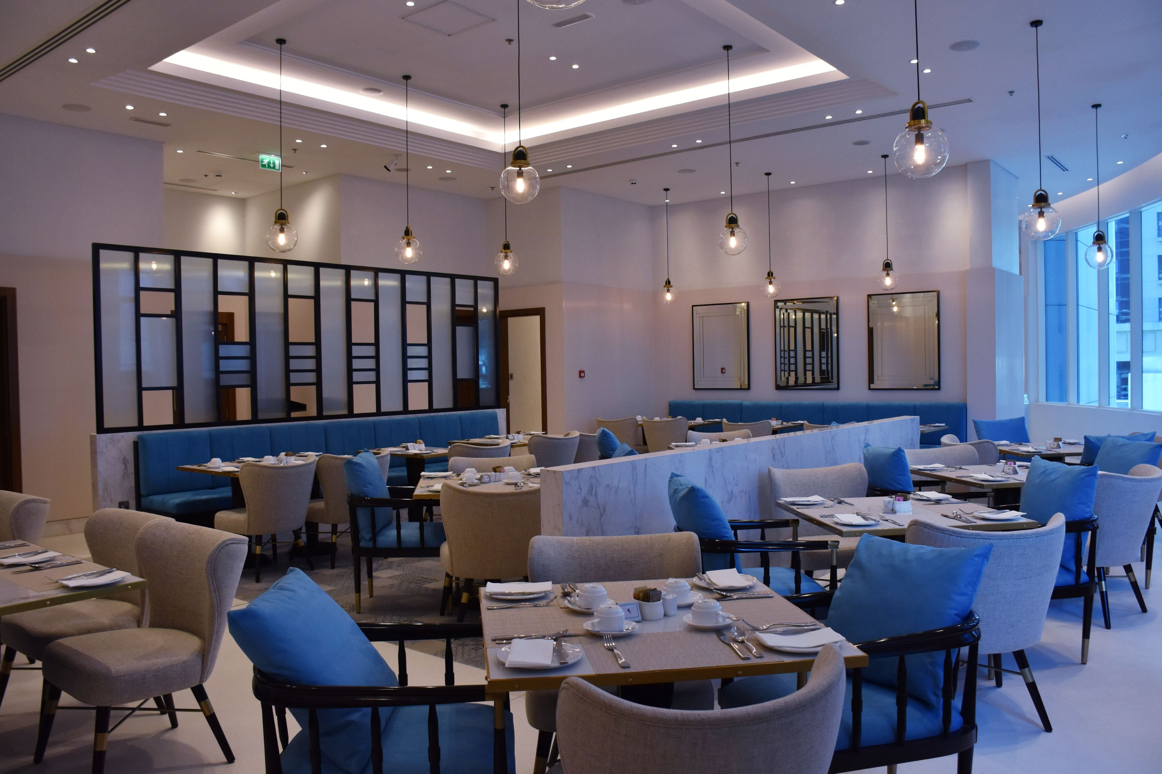 A modern restaurant with round tables, blue cushioned chairs, and pendant lighting.