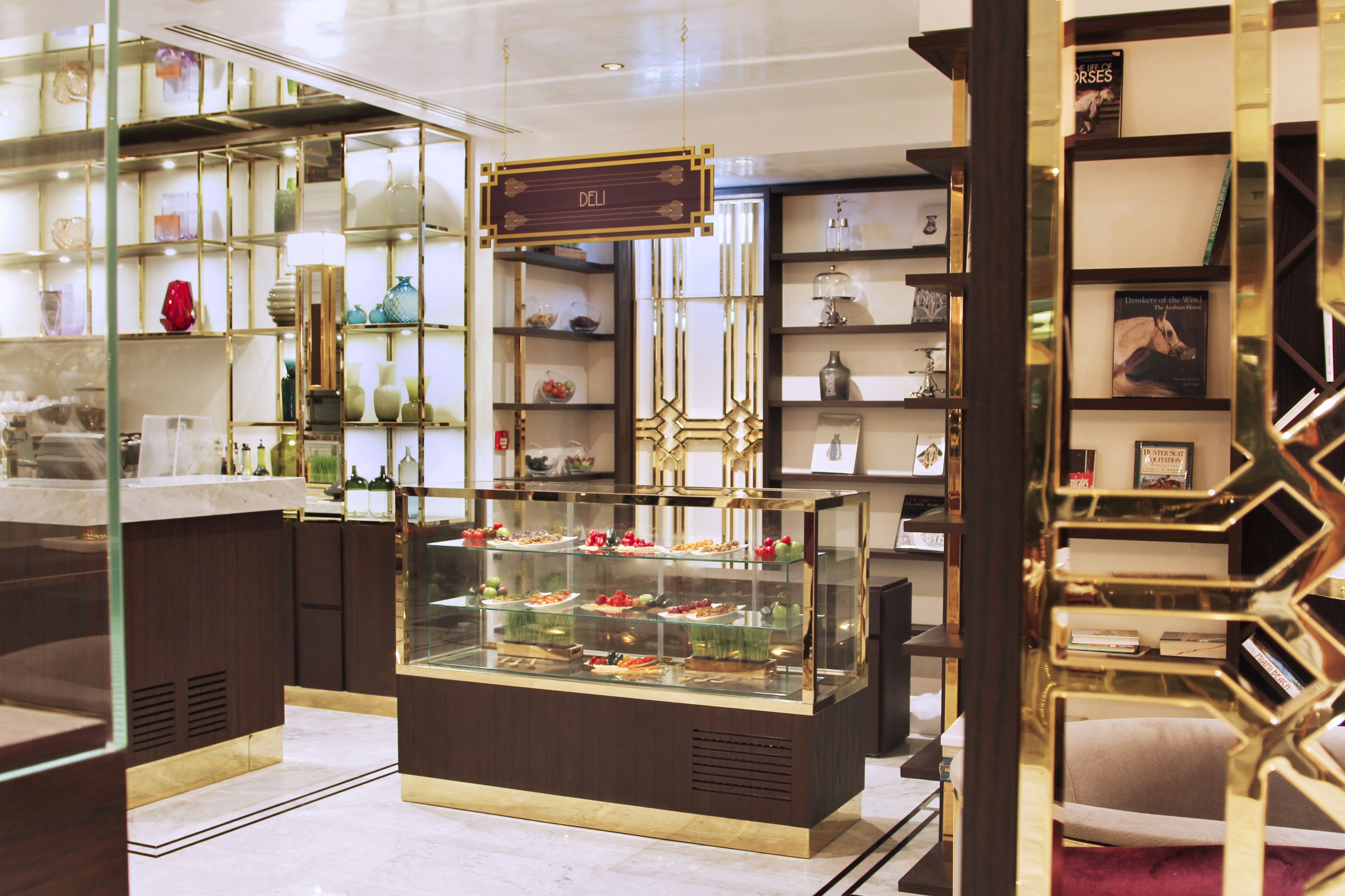 A well-lit, modern interior with a central display case of desserts, surrounded by shelves with various items.