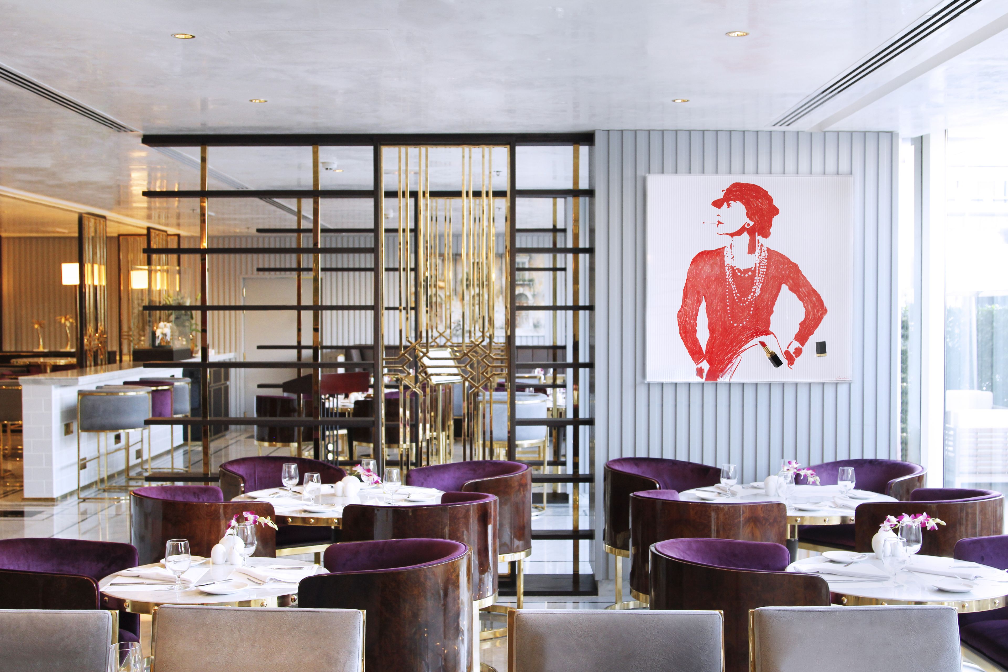 Een moderne eetruimte met paarse stoelen en ronde tafels, een groot raam en een decoratief kunstwerk aan de muur.