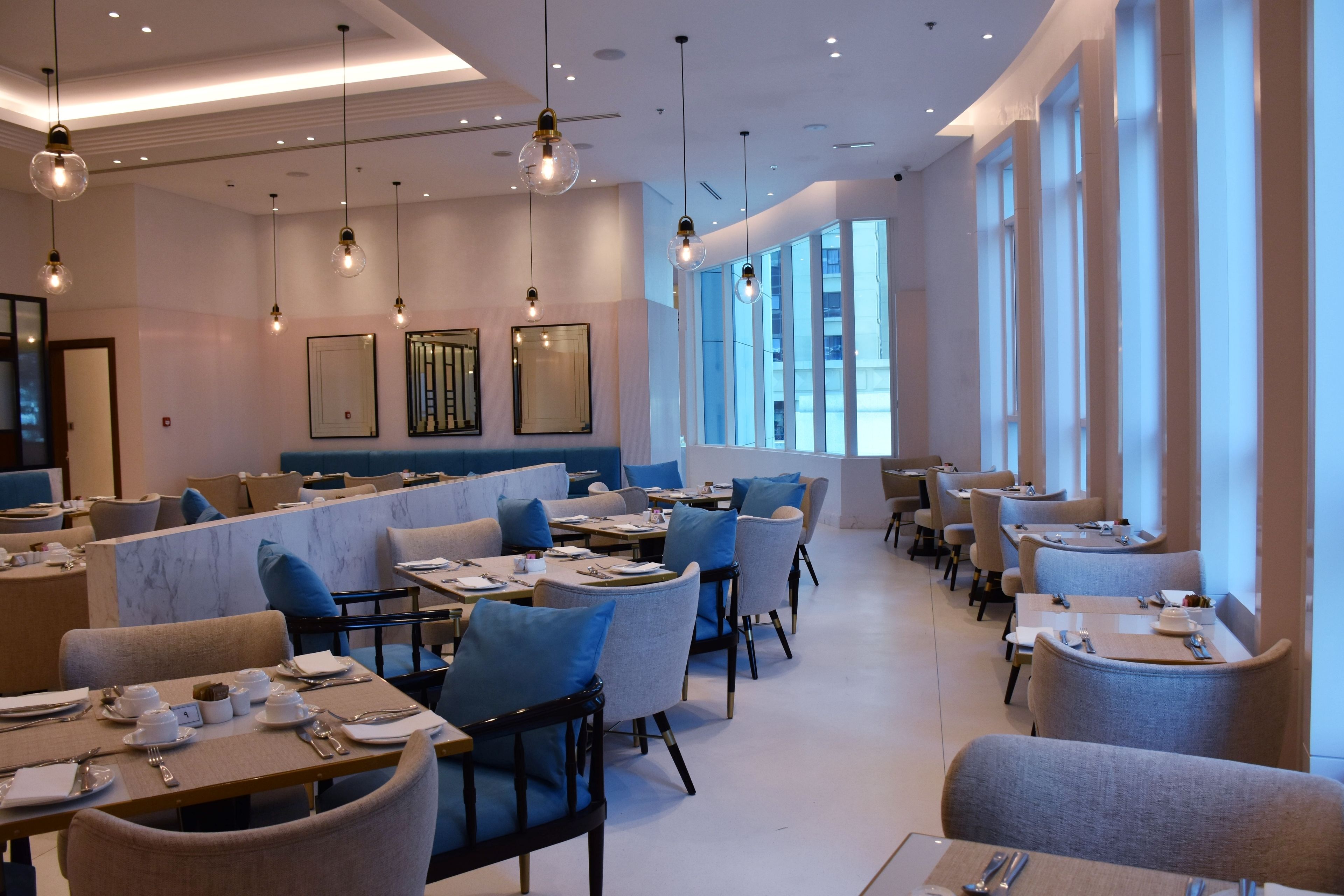 A modern dining area with tables set for service, large windows, and hanging light fixtures.
