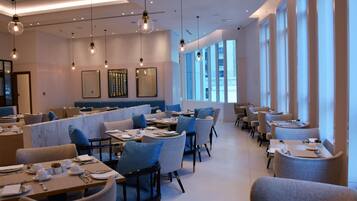 A modern dining area with tables set for service, large windows, and hanging light fixtures.