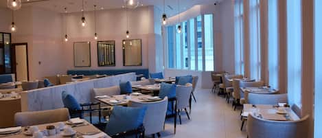 A modern dining area with tables set for service, large windows, and hanging light fixtures.