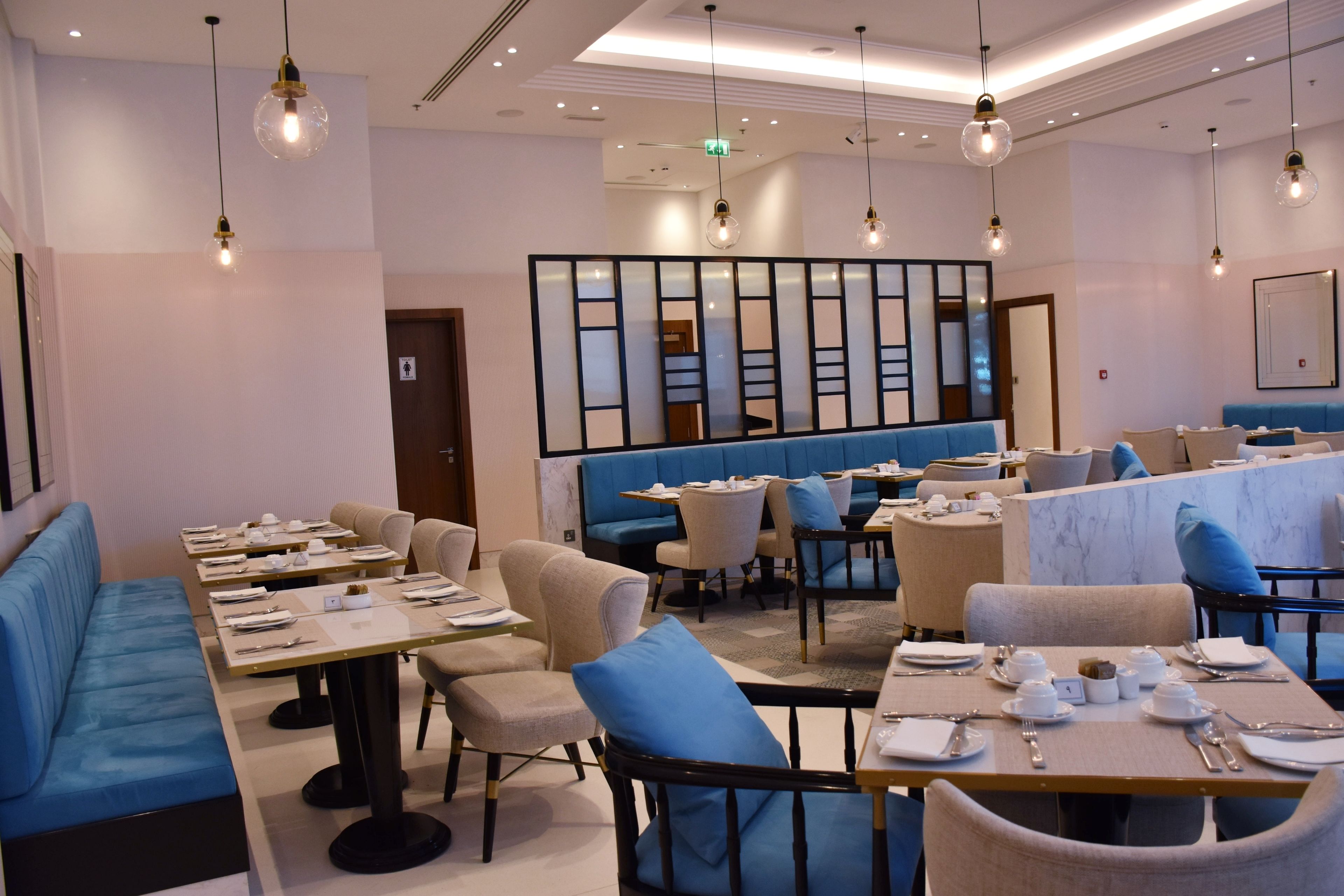 Un espace de restauration moderne avec des sièges bleus, des tables dressées avec de la vaisselle blanche et des luminaires suspendus.
