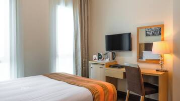 A hotel room with a bed, a desk, a chair, a television, a lamp, and a window with curtains.