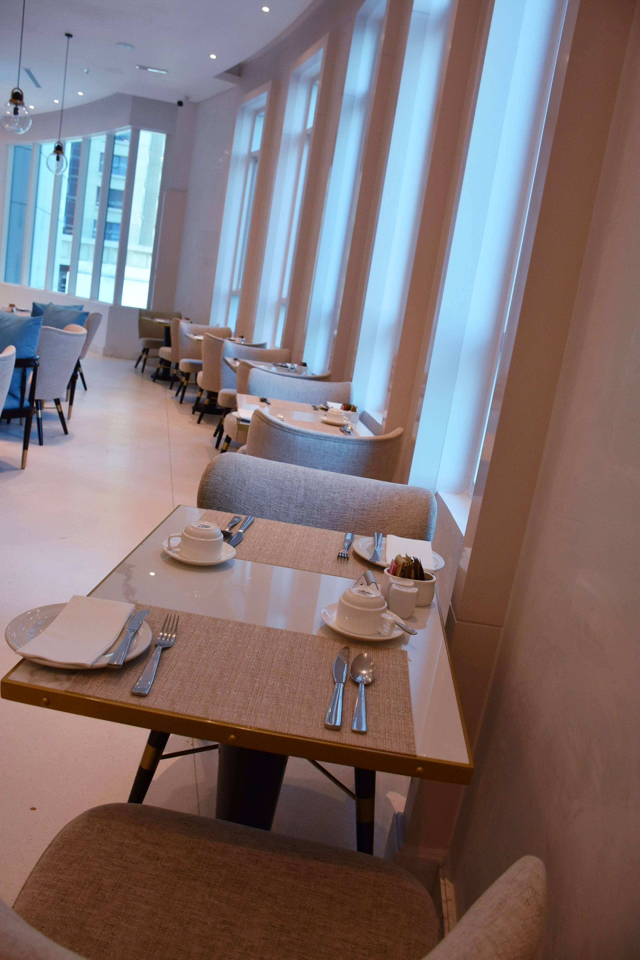 A modern dining area with tables set for two, featuring a neutral color palette and contemporary furniture.