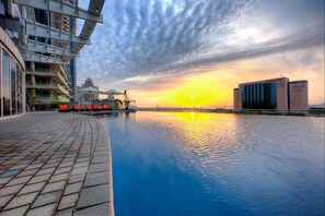 A swimming pool with a sunset view, modern buildings, and a clear sky.