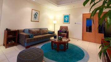 A living room with a sofa, armchair, coffee table, and a large potted plant.