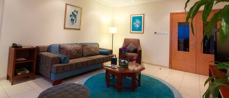 A living room with a sofa, armchair, coffee table, and a large potted plant.