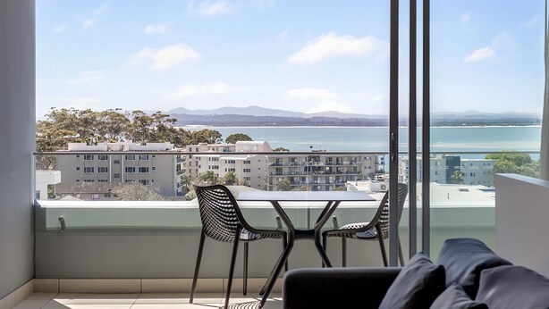Varanda com mesa e cadeiras, vista para um horizonte costeiro com edifícios e um corpo de água.