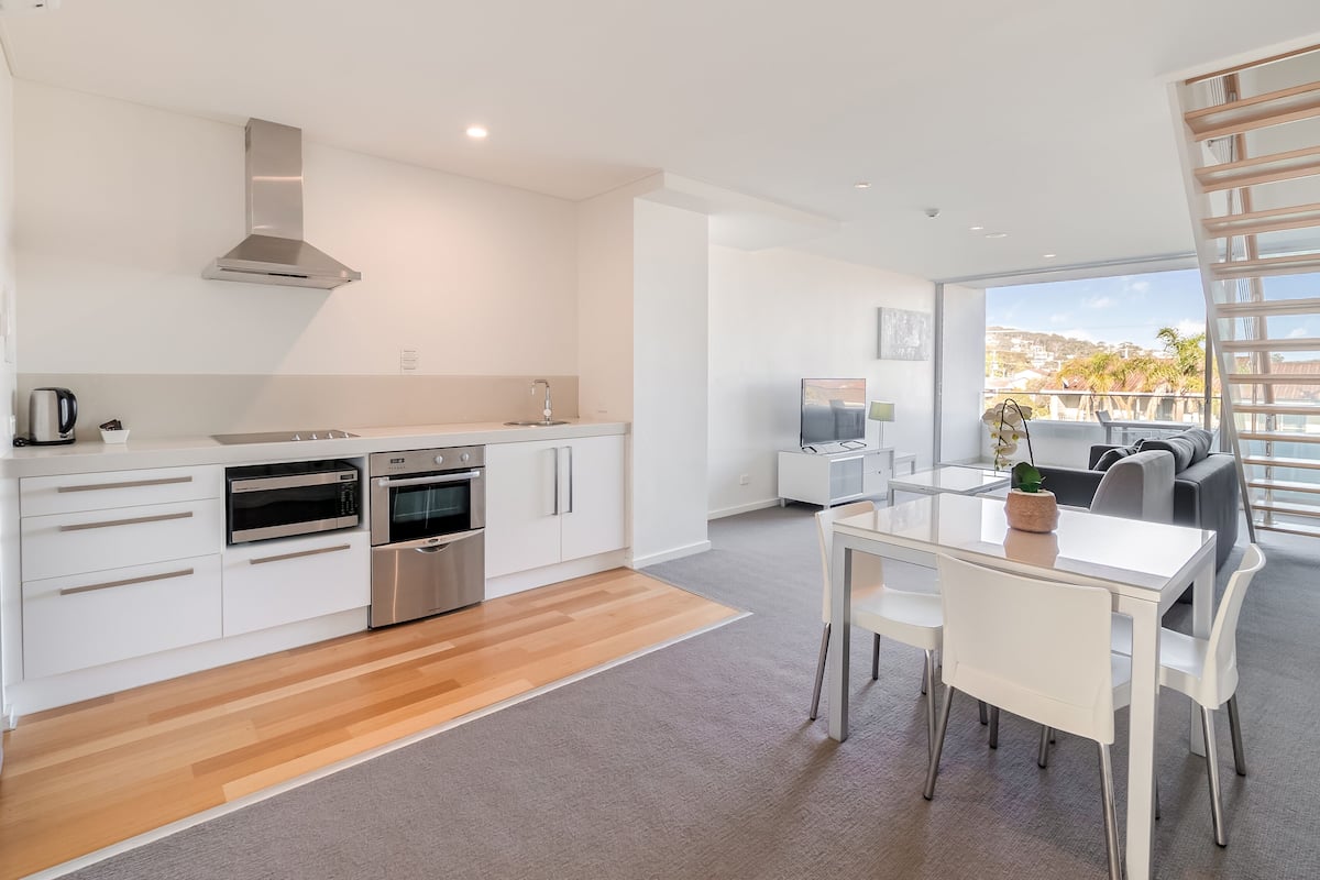 A modern kitchen with white cabinetry, stainless steel appliances, and a dining area with a glass table and chairs.