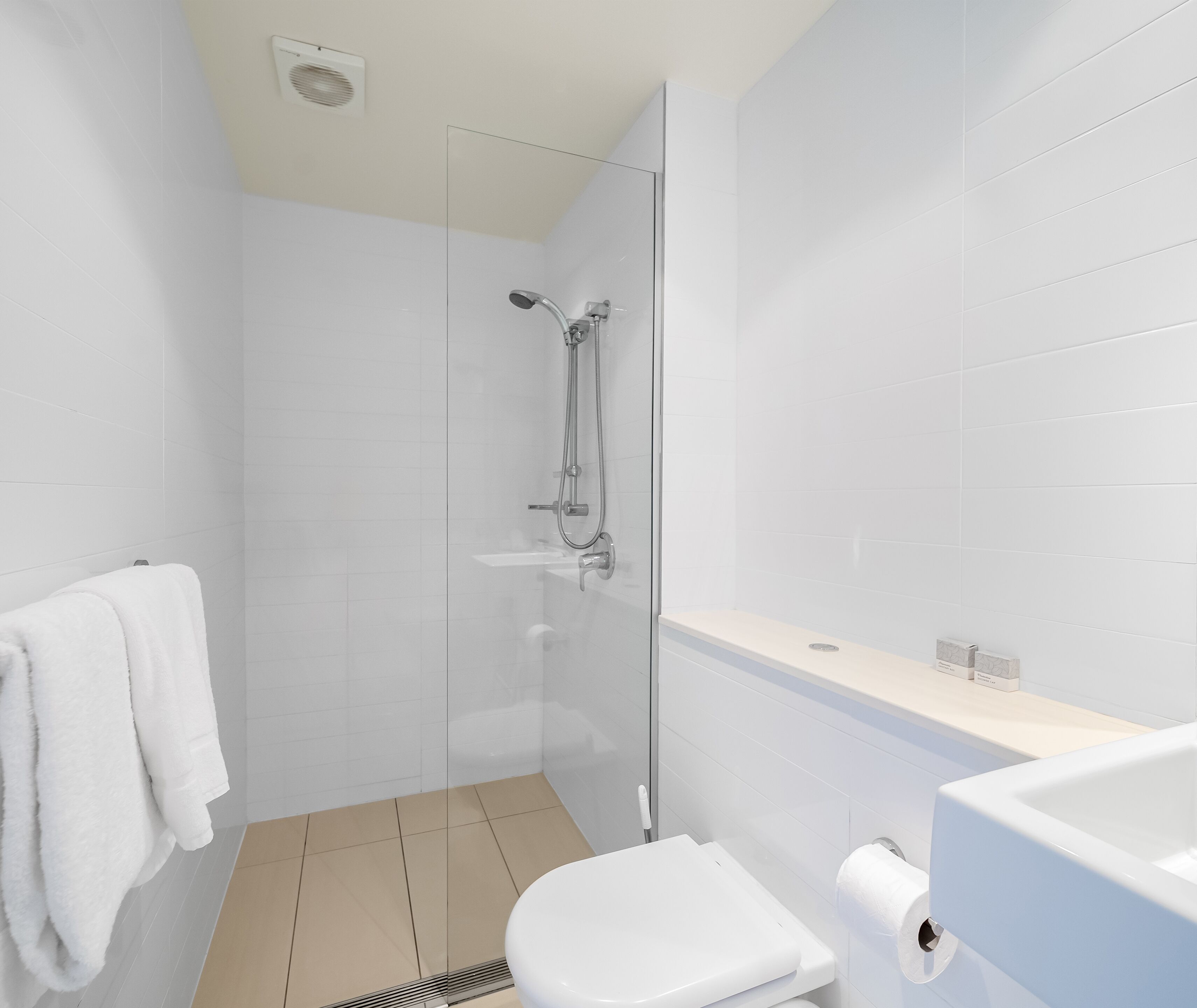 Un baño moderno con cabina de ducha de vidrio, inodoro blanco y lavamanos con espejo.