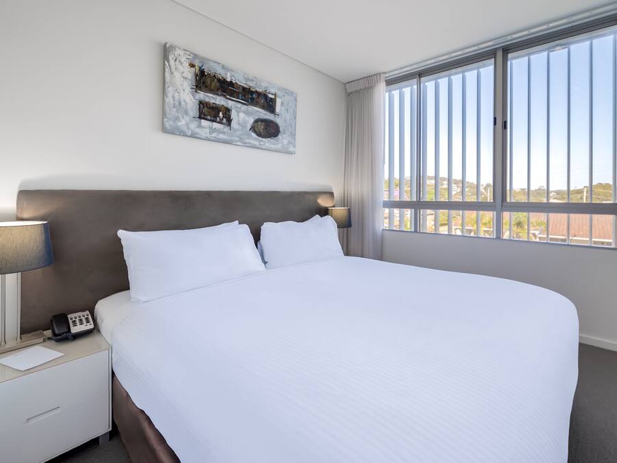 A hotel room with a large bed, a bedside table with a lamp, a phone, and a painting on the wall.