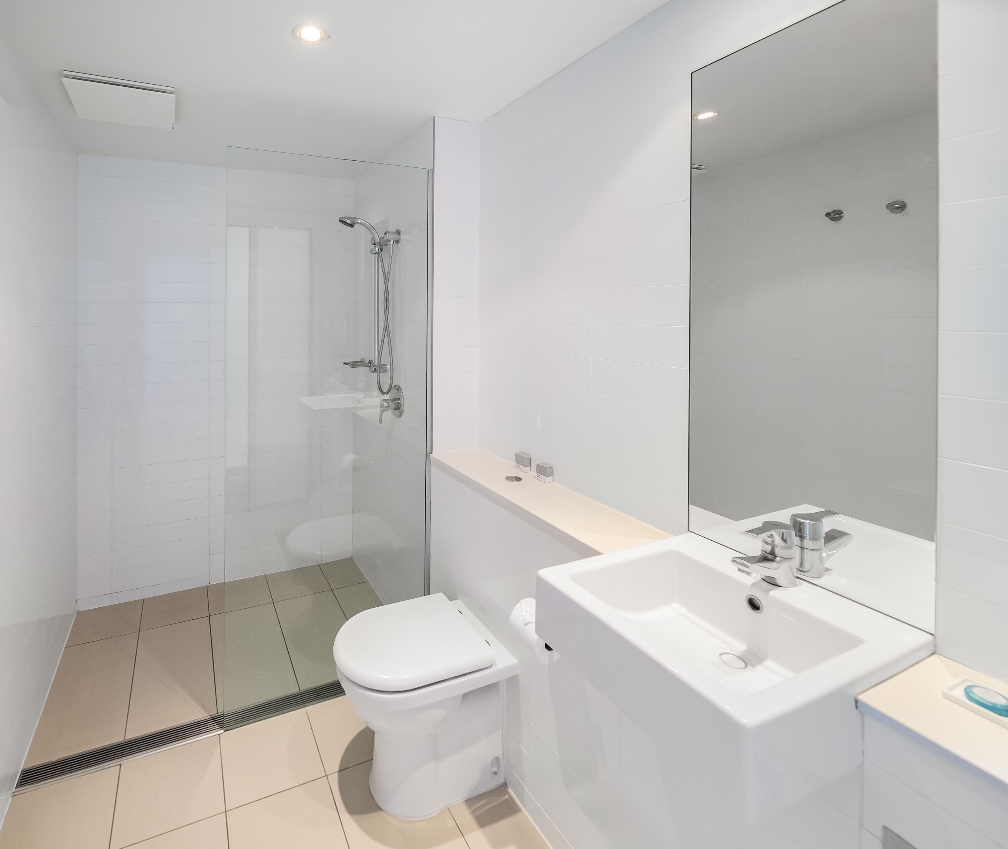Une salle de bain moderne avec une douche à parois de verre, des toilettes blanches et un grand miroir au-dessus d’un lavabo blanc.