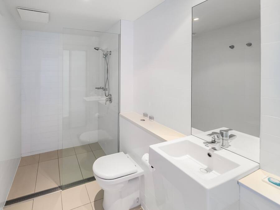 A modern bathroom with a glass-enclosed shower, a white toilet, and a large mirror above a white sink.