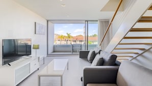 Uma sala de estar moderna com uma televisão de tela plana, uma mesa de centro branca e um sofá cinza.
