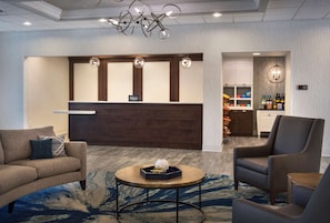 A hotel lobby with a reception desk, seating area, and a bar.
