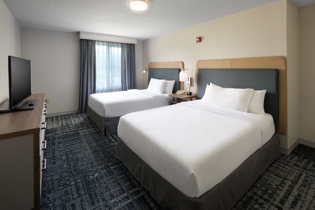 A hotel room with two beds, a desk with a TV, and a window with curtains.