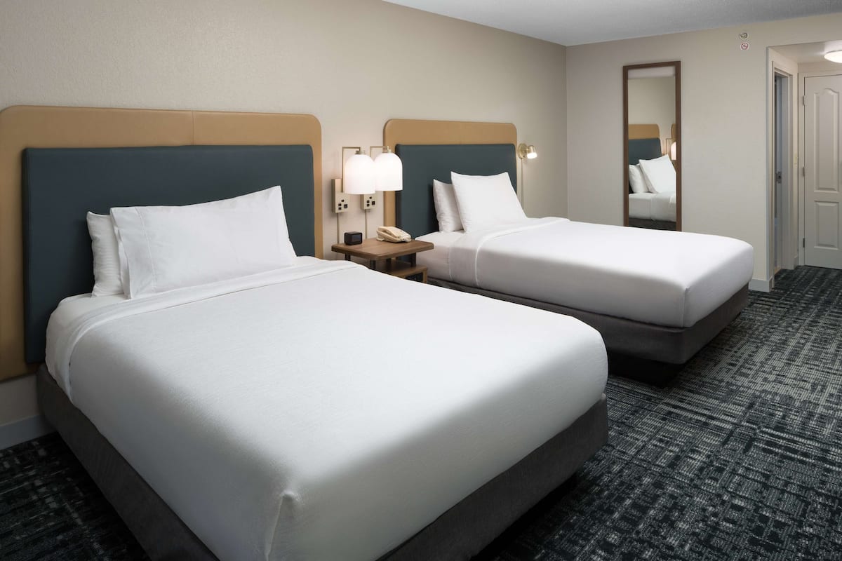 A hotel room with two beds, a nightstand with a phone, and a mirror.