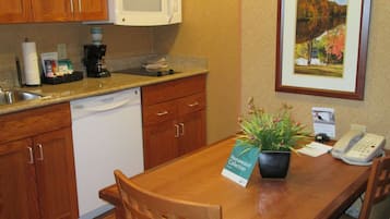 Una cocina compacta con armarios de madera, microondas integrado, cafetera y una pequeña mesa de comedor con planta en maceta.