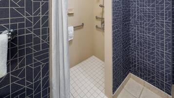 Un baño con un patrón geométrico de azulejos, un perchero, un cabezal de ducha y un dispensador de papel higiénico.