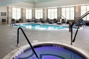 A hotel indoor pool with lounge chairs, a hot tub, and a warning sign.