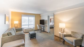 Hotellihuone, jossa on sohva, työpöytä tietokoneella, televisio ja lamppu.