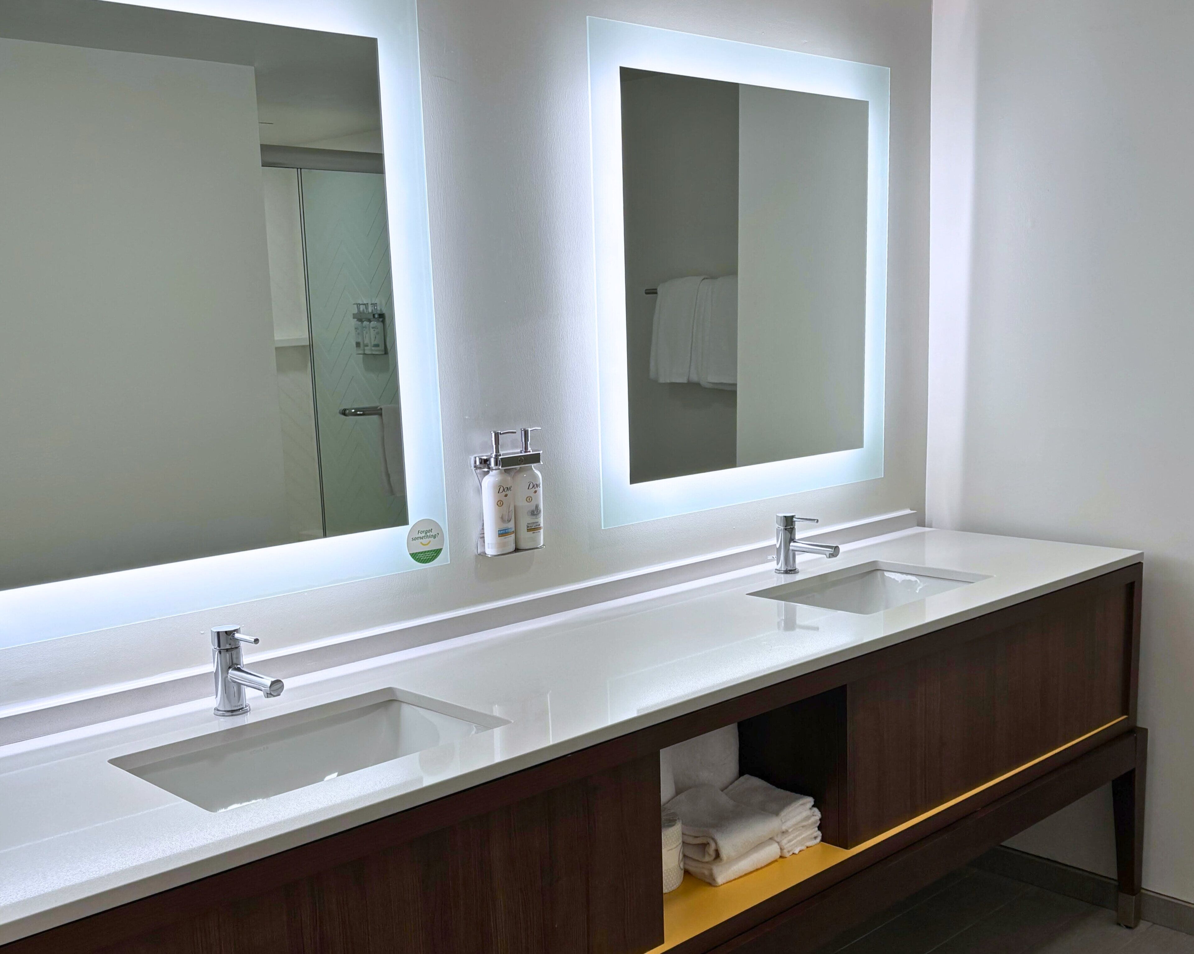 Une salle de bain moderne avec deux vasques, un grand miroir et un meuble-lavabo en bois doté d’un porte-serviettes.