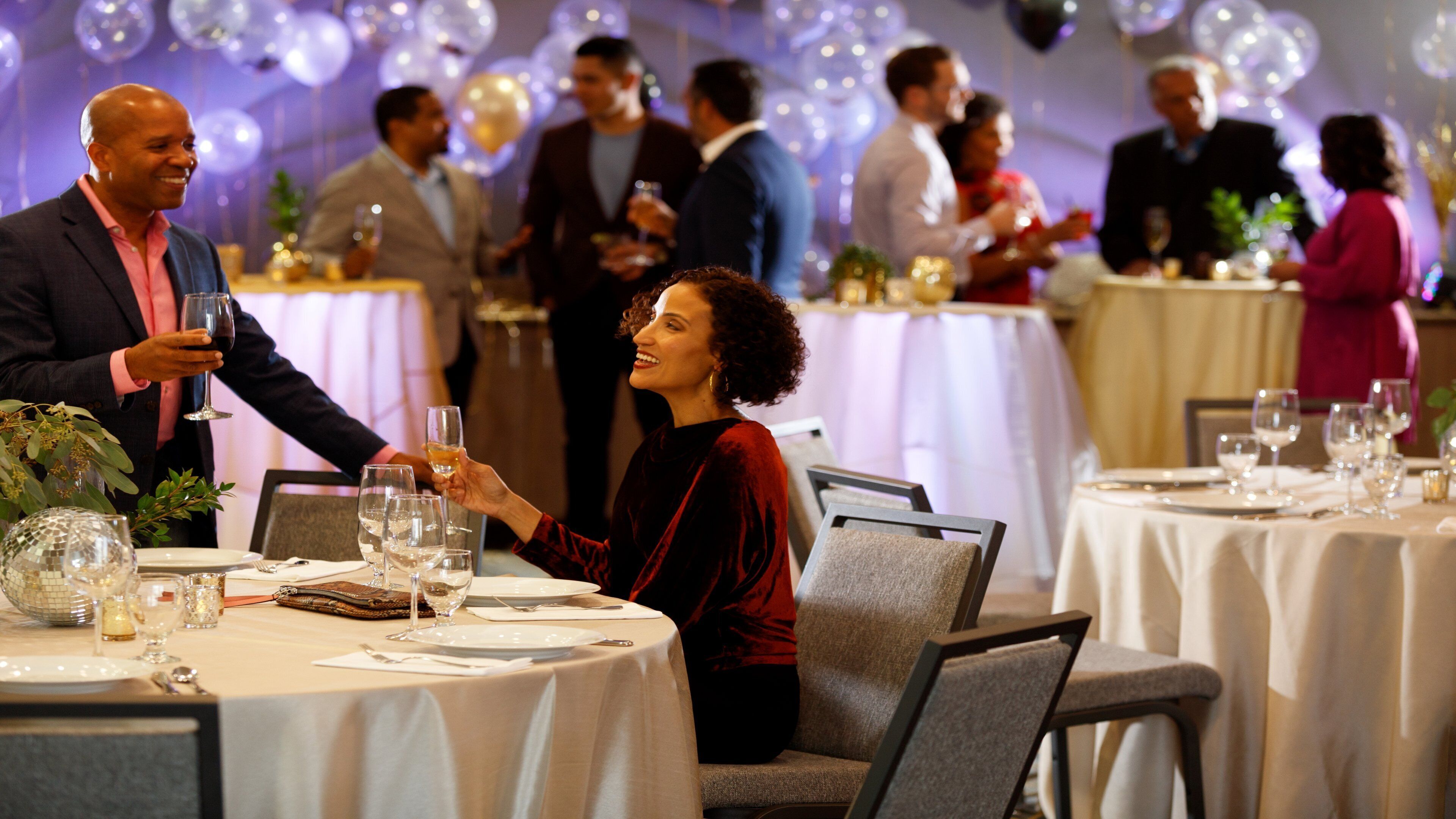 A formal dining setting with round tables, chairs, and guests engaged in conversation.