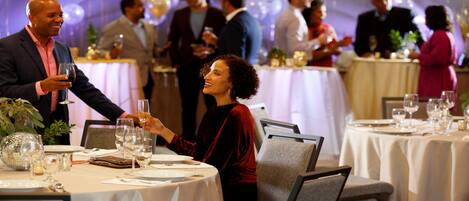 A formal dining setting with round tables, chairs, and guests engaged in conversation.