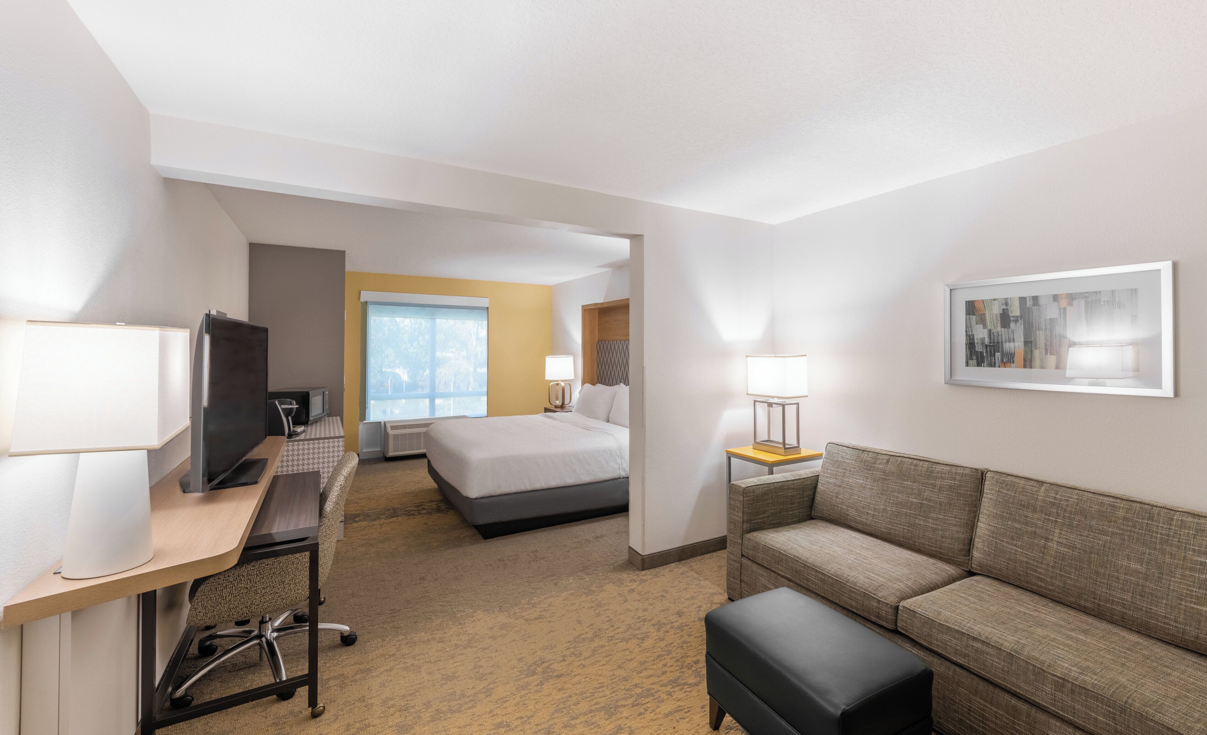 A hotel room with a bed, a desk with a computer, a couch, and a TV.