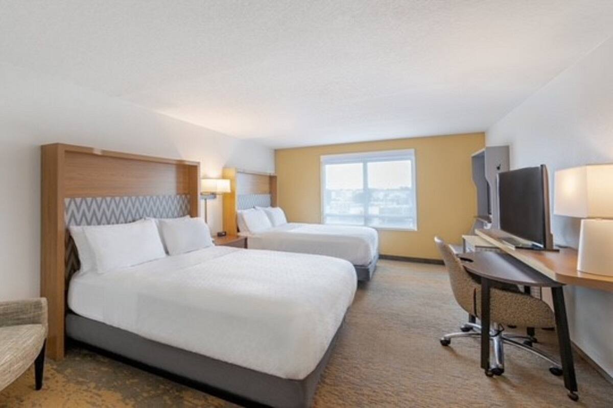 A hotel room with two beds, a desk with a computer, a TV, and a chair.
