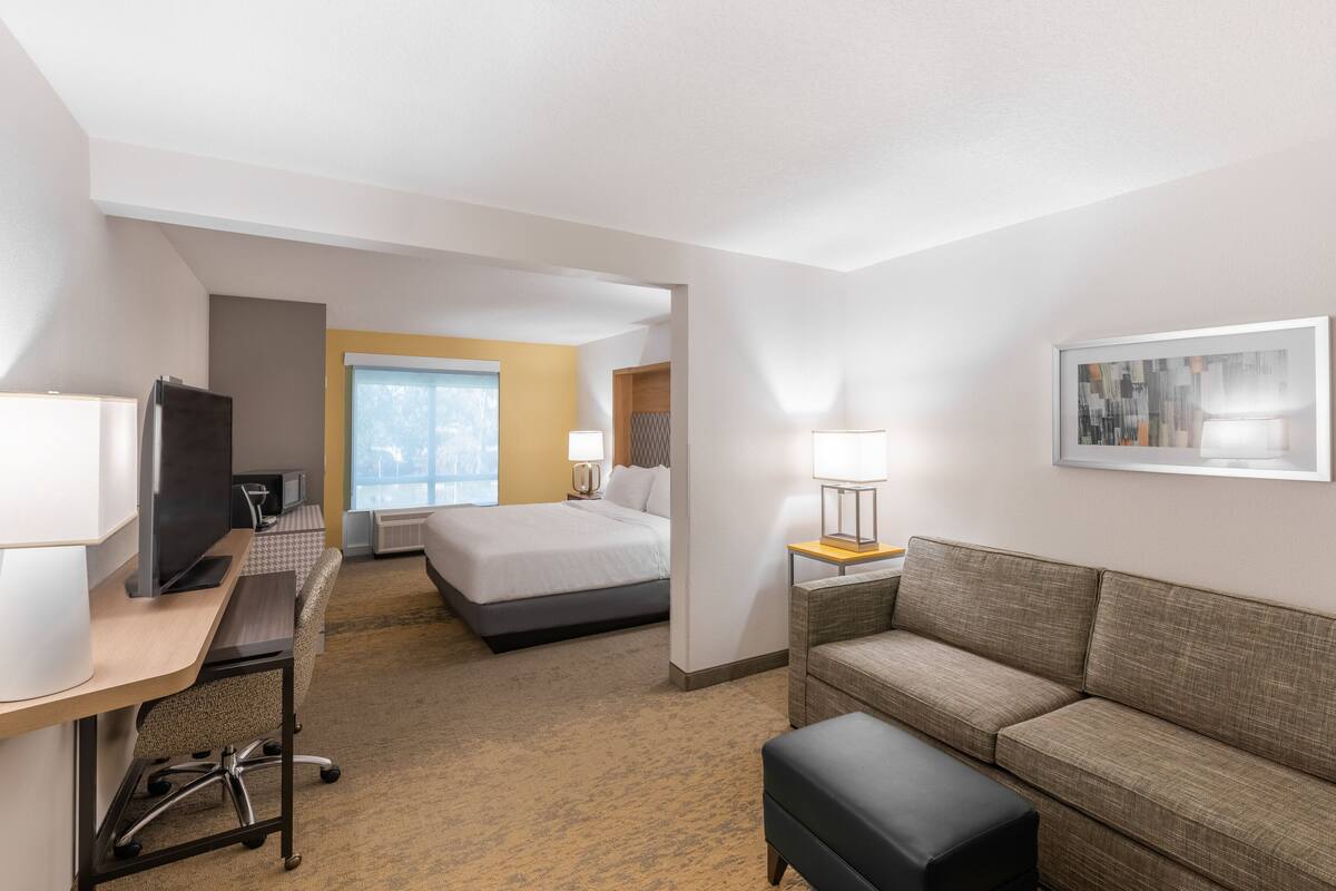 A hotel room with a bed, a desk with a computer, a TV, a sofa, and a lamp.