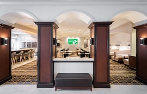 A hotel lobby with a reception desk, seating area, and a large green sign.