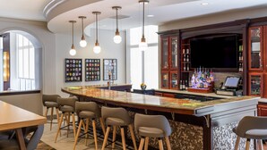 Un espace bar doté d’un comptoir incurvé, de tabourets de bar, de luminaires suspendus, d’un téléviseur à écran plat et d’une étagère où sont exposées des bouteilles.