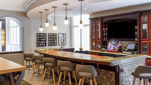 Zona de bar con barra curva, taburetes, iluminación colgante, un televisor de pantalla plana y una exhibición de botellas.