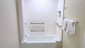 Une salle de bain avec un mur de douche orné d’un motif en chevrons blancs, une baignoire blanche et un porte-serviettes avec des serviettes.