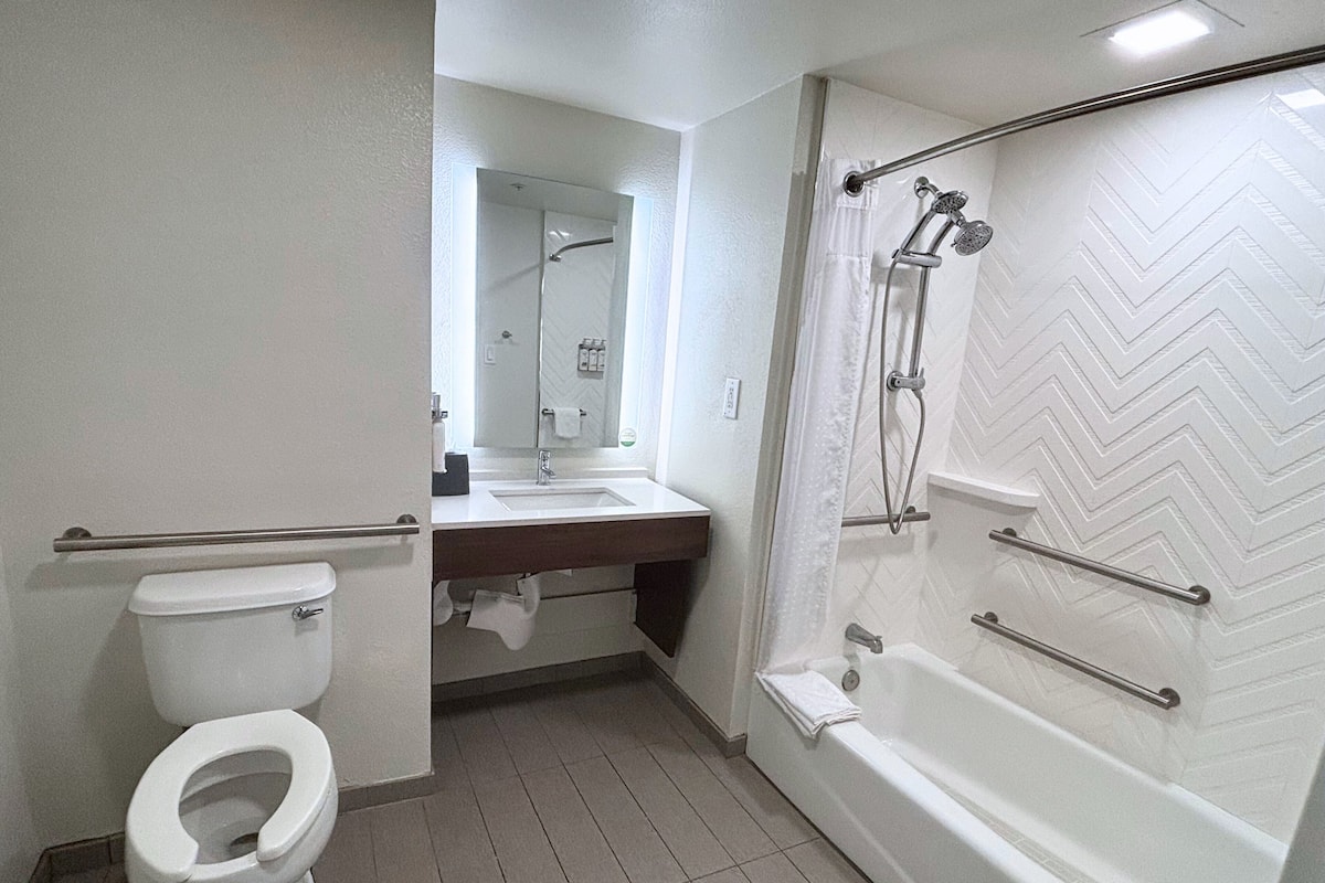 A bathroom with a toilet, sink, mirror, shower, and tiled floor.