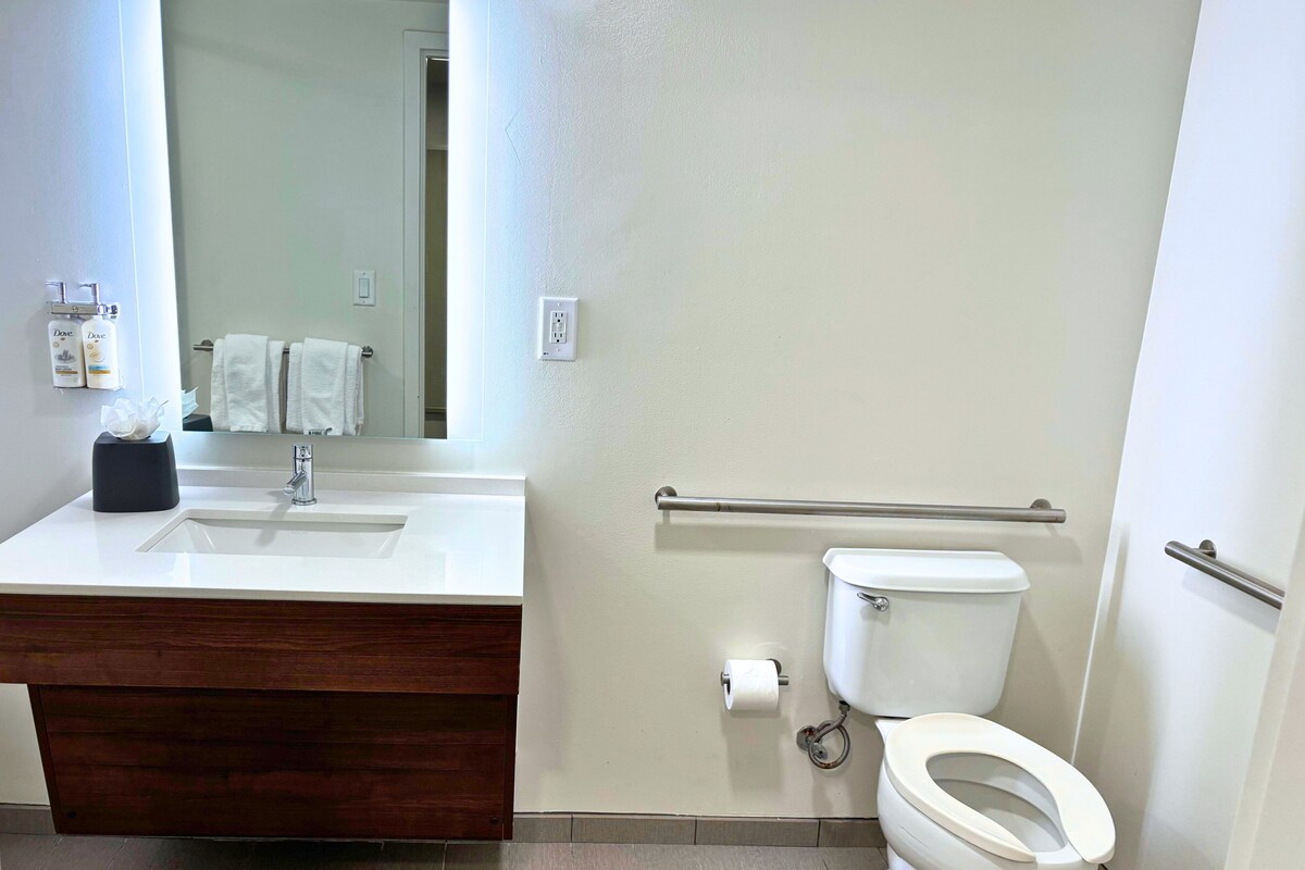 Een badkamer met een wit wastafel, een spiegel, een toilet en een handgreep.