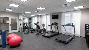 Une salle de sport équipée de tapis de course, de vélos elliptiques et d’un ballon d’exercice rouge.