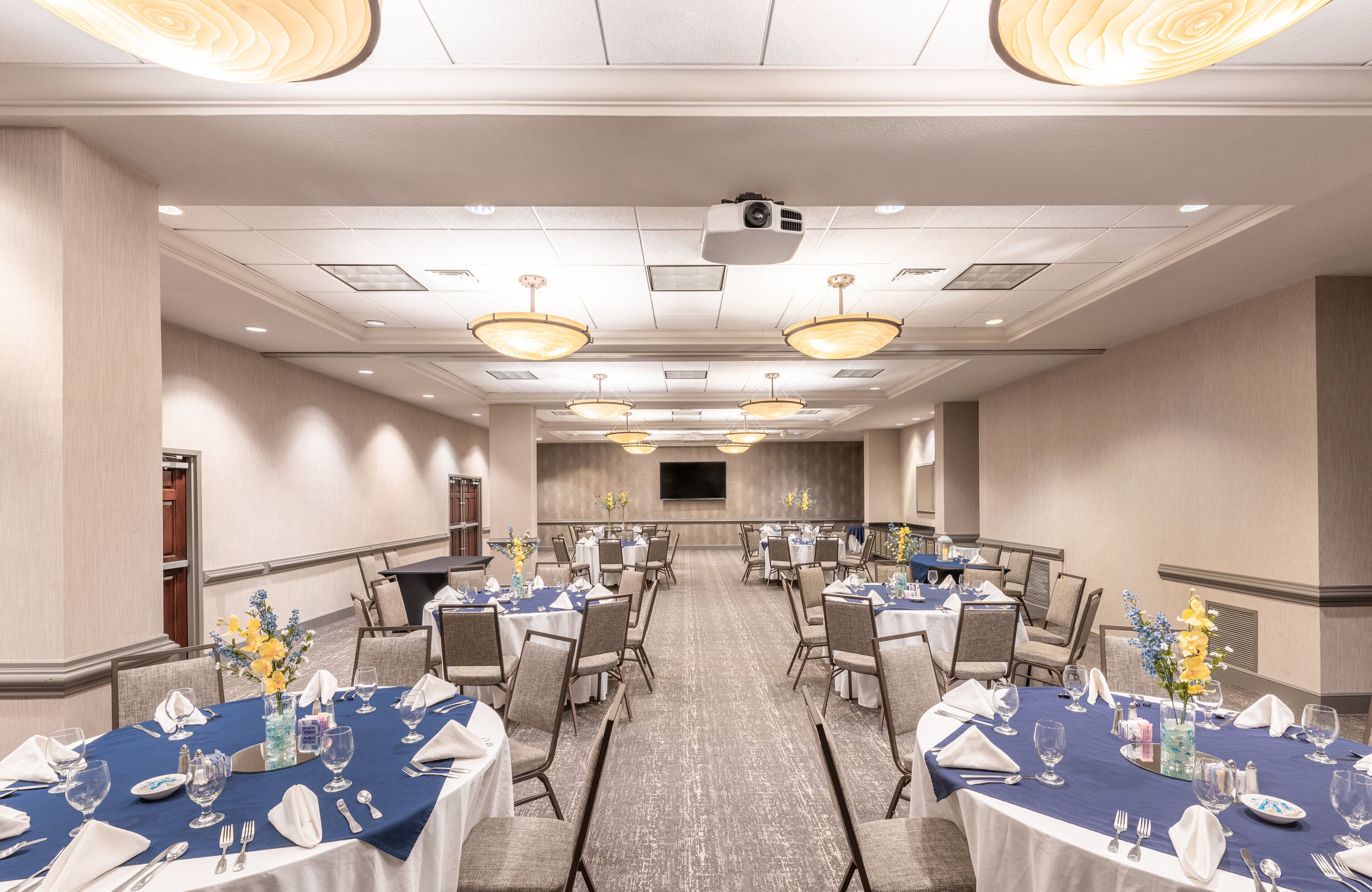 A conference room with round tables, chairs, and a projector screen.