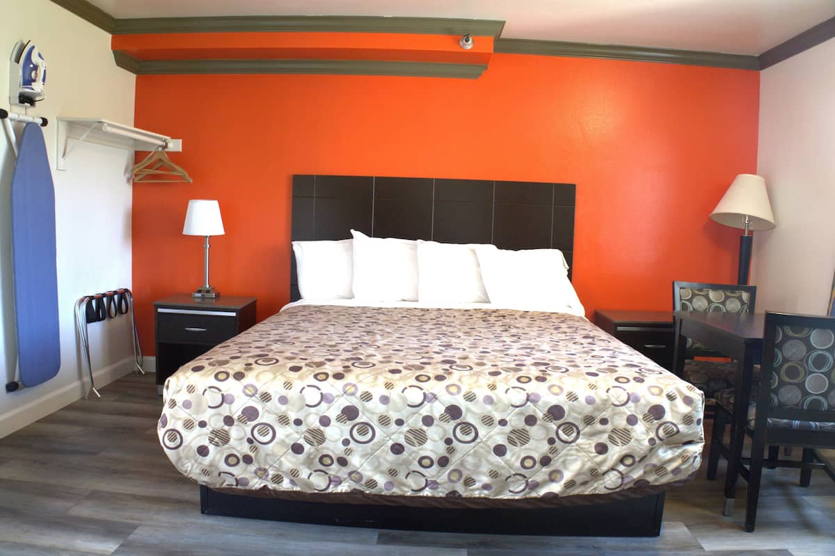 Una habitación de hotel con una cama grande, una mesita de noche, una silla y un escritorio con una lámpara.