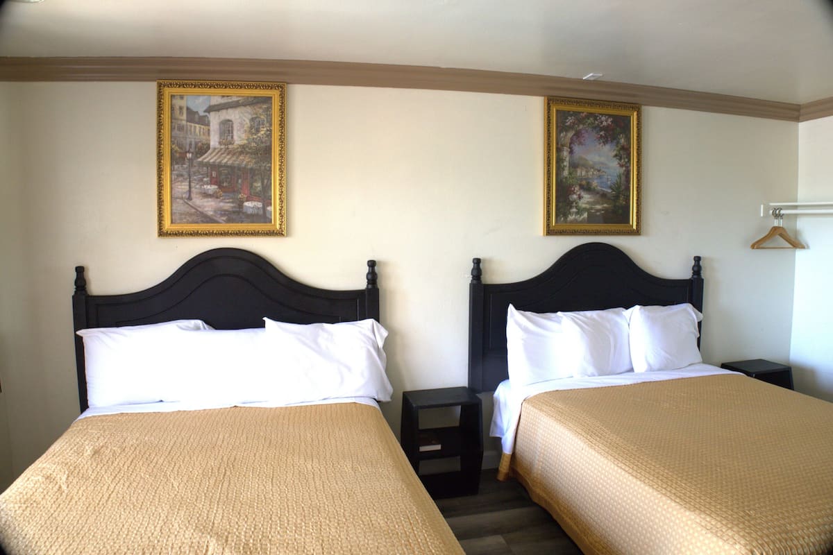 Habitación de hotel con dos camas, cada una con cabecera, mesita de noche y perchero.