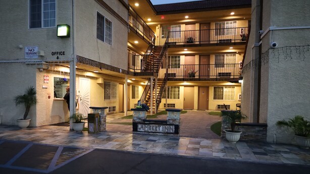 A multi-story building with a central staircase, outdoor seating area, and a sign indicating an office. - Lambert Inn (Whittier)