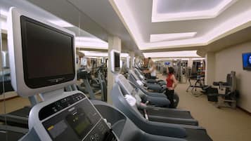 Un gimnasio con cintas de correr, equipo de ejercicio y una pantalla de televisión.