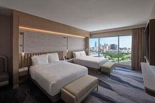 Habitación de hotel con dos camas, vistas a la ciudad y un ventanal grande.