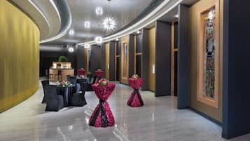 A modern hotel lobby with a bar area, round tables, and decorative floral arrangements.