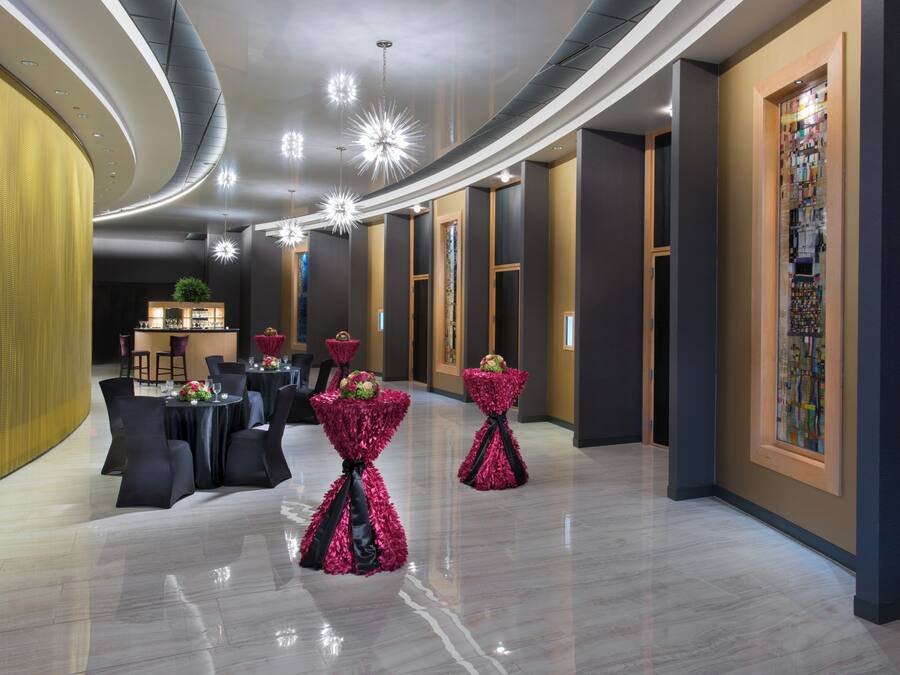 A modern hotel lobby with a bar area, round tables, and decorative floral arrangements.